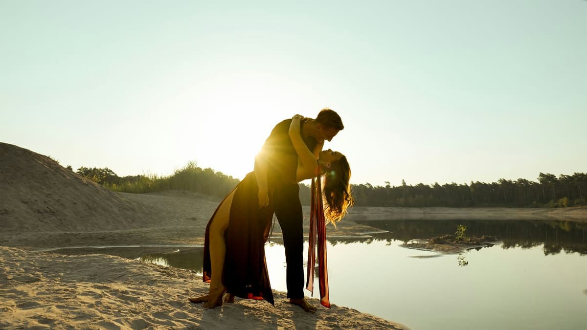 A couple embracing passionately in a romantic sunset setting by the lake.