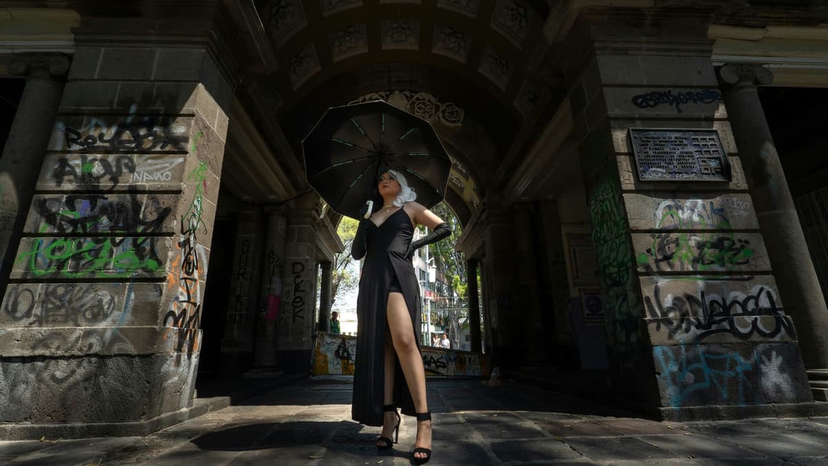 Elegant woman with black umbrella in a graffiti-adorned archway, Mexico City.