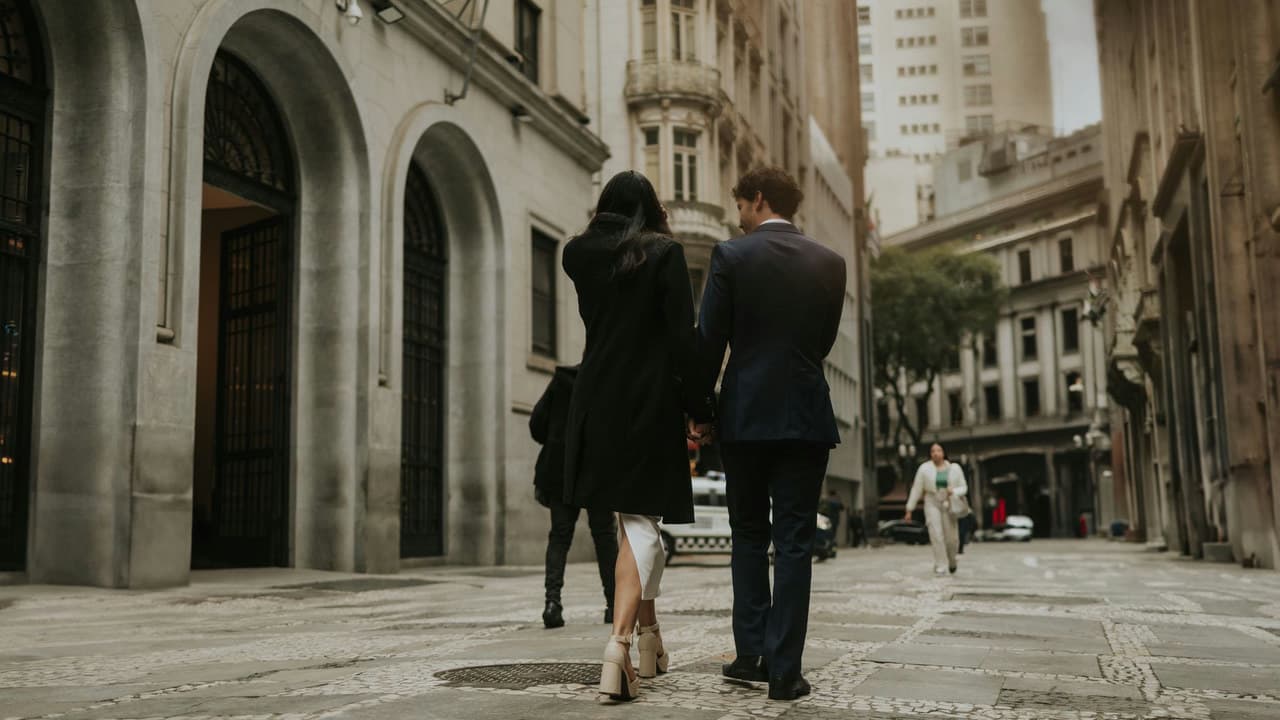 A stylish couple strolls through a historic city street surrounded by iconic architecture.