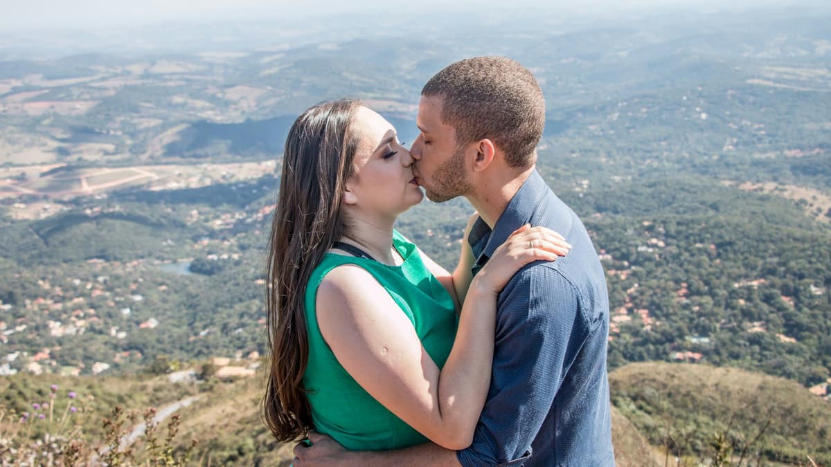 A couple shares a romantic kiss with a breathtaking view of Belo Horizonte's mountainous landscape.